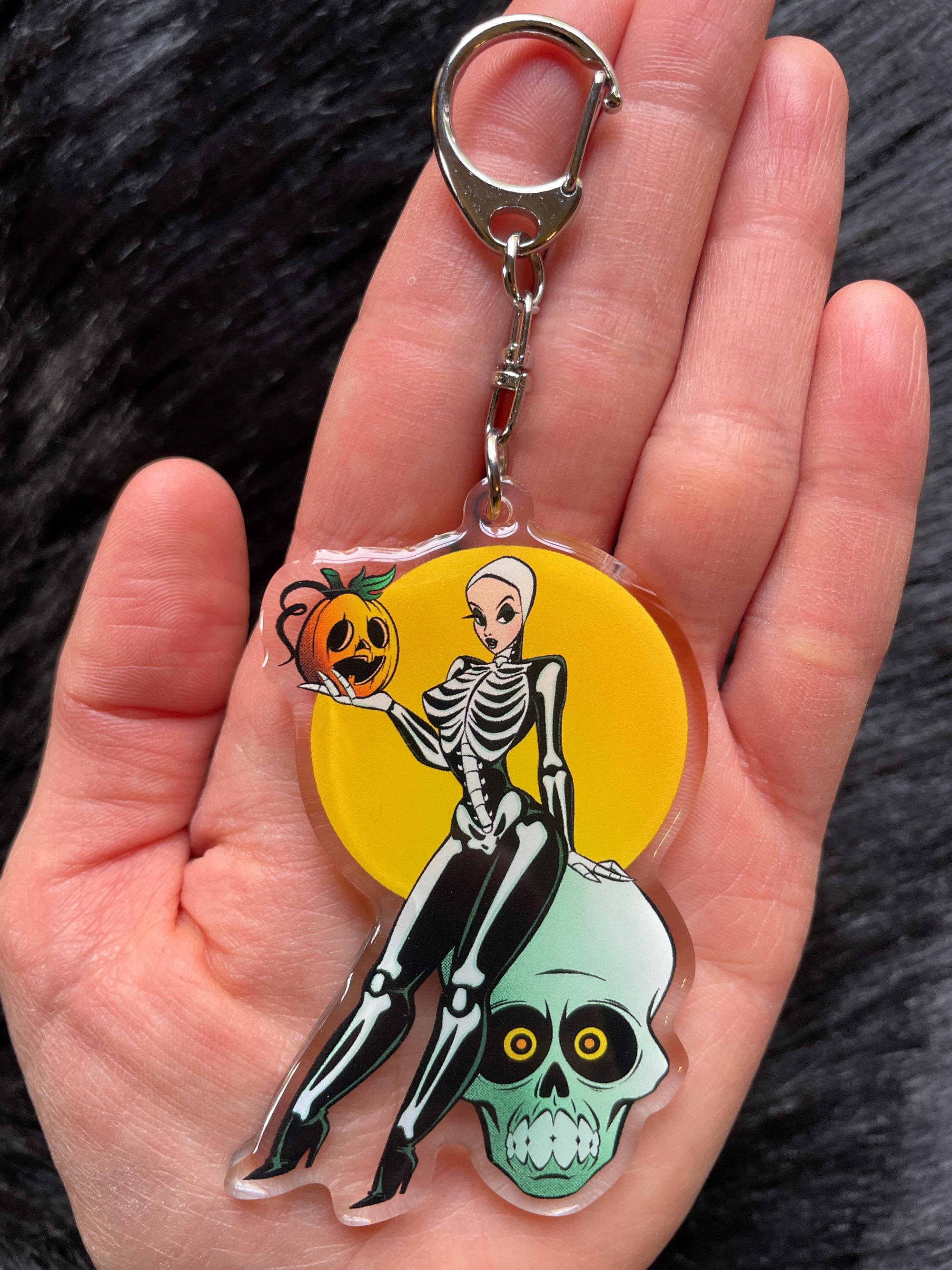 clear acrylic keychain with skeleton pinup sitting on skull keychain
